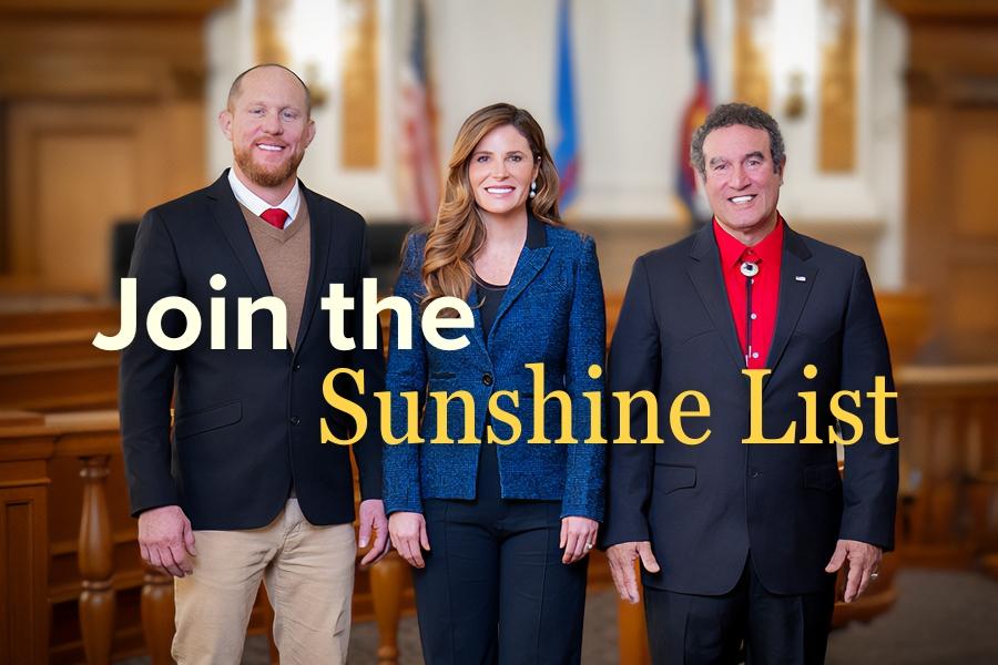 One woman standing in the middle of two men (Board of Mesa County Commissioners) in professional clothing smiling with white and yellow text reading Join the Sunshine List.